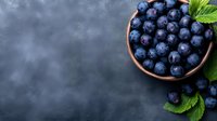 Fresh ripe blueberries in wooden bowl with green leaves on dark moody background, copy space for text. Food photography styling.