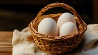 Fresh white chicken eggs in rustic woven basket on wooden table with natural linen cloth, warm lighting creates cozy farmhouse atmosphere.