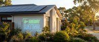 Modern eco-friendly house with solar panels and energy rating sign surrounded by native landscaping during golden hour sunset lighting.