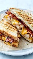 Grilled sandwich with melted cheese, crispy bacon and sliced turkey on toasted bread served on white plate for comfort food and deli menu concepts.