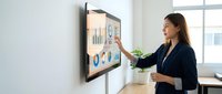 Professional businesswoman presenting financial data on interactive touchscreen display in modern office environment for corporate meetings and presentations.