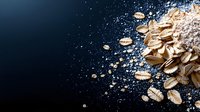 Scattered raw oats and grains on dark background with flour dust creating dramatic food composition for healthy breakfast and baking concept.