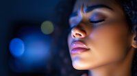 Close-up portrait of young African American woman with closed eyes in blue night lighting, showcasing serene facial expression and glossy lips.