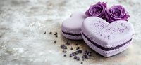 Heart shaped purple macarons with lavender filling decorated with purple roses and sprinkles on rustic concrete background, romantic food photography.