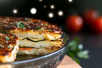 Layered potato gratin with golden crispy crust, melted cheese and herbs in glass baking dish. Selective focus on crusty edge with bokeh lights background.