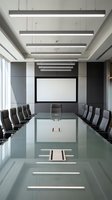 Modern corporate boardroom with glass conference table and suspended linear LED lighting fixtures for business meetings and presentations.
