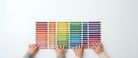 Hands arranging colorful paint sample strips in rainbow spectrum on white surface for interior design and color selection projects.