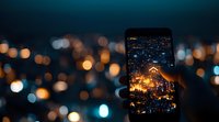 Smartphone screen capturing illuminated cityscape at night with bokeh lights in background, creating atmospheric urban photography composition.