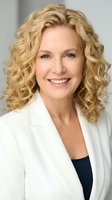 Professional mature blonde woman in white blazer smiling confidently at camera for business portrait and corporate headshot photography.