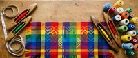 Colorful quilting fabric with geometric pattern surrounded by sewing supplies including thread spools, scissors and measuring tape on wooden surface.