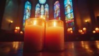 Glowing candles in church interior with colorful stained glass windows creating atmospheric spiritual ambiance.