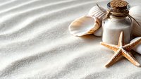 Glass bottle with cork stopper, seashell and starfish on sandy beach with shadow patterns. Coastal decoration and marine spa concept.