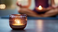Glowing candle in textured glass holder creates cozy atmosphere with warm light and soft bokeh background, perfect for relaxation and mindfulness moments.