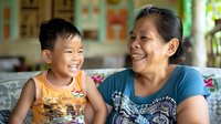 Asian grandmother and grandson sharing joyful laughter moment at home, authentic emotional connection between generations showing family bonds and happiness.