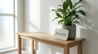 Minimalist wooden console table with green potted plant and welcome sign near bright window, cozy home interior decor concept.