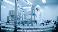 Pharmaceutical technician in protective suit operating automated filling equipment in sterile cleanroom manufacturing facility for drug production.