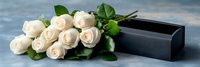 White roses bouquet with green leaves lying beside elegant black gift box on marble surface for romantic occasions and special celebrations.