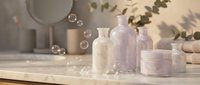 Spa wellness skincare products with soap bubbles on wooden surface. Natural beauty treatment bottles, jars and towels in serene bathroom setting.