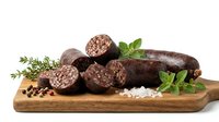 Traditional blood sausage slices on wooden cutting board with fresh herbs and spices, isolated on white background for culinary design projects.