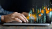 Close-up of hands typing on laptop keyboard with glowing financial charts and stock market data visualization overlay, illustrating digital trading and analysis.