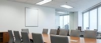 Modern corporate boardroom with large conference table and executive chairs overlooking city skyline through floor-to-ceiling windows for business meetings.