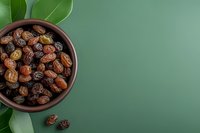 Fresh organic dates in brown ceramic bowl on green background with tropical leaves, top view with copy space for healthy eating concept.