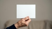 Senior male hand holding blank white card against neutral background, suitable for advertising, marketing campaigns, business messaging, and promotional materials.