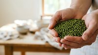 Caucasian male farmer or agricultural worker holding fresh green lentils in hands over wooden table with harvest produce, showcasing organic legume crop for cooking and nutrition.
