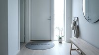 Bright minimalist entryway with welcome mat, white door, orchid plant, round mirror, and wooden bench in a modern Scandinavian home interior.