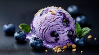 Creamy blueberry ice cream scoop with fresh berries, mint leaves and crushed cookies on dark background, selective focus with soft bokeh effect.