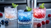 Colorful summer cocktails in crystal glasses with fresh berries and mint garnish. Refreshing drinks with ice cubes arranged on dark surface, professional mixology.