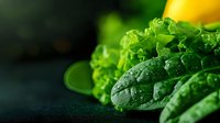 Fresh wet spinach leaves with water drops in dark moody setting, macro photography of green organic vegetables for healthy eating and nutrition concept.