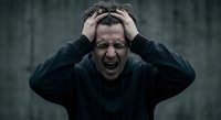 Stressed middle-aged Caucasian man screaming with hands on head expressing mental breakdown, anxiety and emotional crisis in dark moody setting.