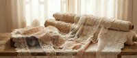 Cozy beige knitted blankets and throws draped over wooden bench near window with soft natural light creating warm comfortable home interior atmosphere.