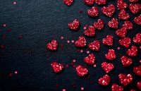 Sparkling red heart-shaped glitter scattered on black slate background, creating romantic Valentine's Day or anniversary decoration.