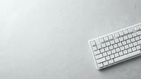 Wireless white keyboard on light gray desk surface with copy space for text, suitable for tech, office, and workspace design projects.