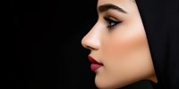 Profile view of young woman with hijab against black background, showcasing defined eyebrows, smoky eye makeup, and deep red lipstick.