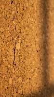 Cracked orange clay wall surface with weathered texture showing natural erosion patterns and rough earthen material for construction and architectural backgrounds.