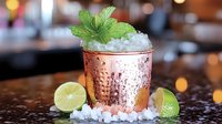 Refreshing Moscow Mule cocktail in copper mug garnished with fresh mint, crushed ice, and citrus slices on dark surface with bokeh lights background.