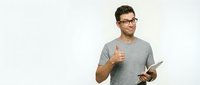Young man with dark hair and glasses wearing gray t-shirt holding tablet, giving thumbs up gesture, isolated on white background for web and marketing use.