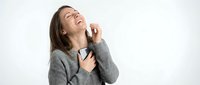 Young woman with dark hair and light skin tone wearing gray sweater, touching neck and looking upward with hand near face, isolated on white background for healthcare and wellness design use.