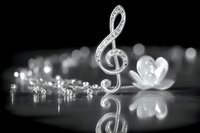 Silver treble clef musical note reflection on dark surface with bokeh lights and delicate white flower, artistic monochrome composition for music themes.