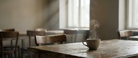 Cozy cafe interior with steaming coffee cup on wooden table, warm natural lighting from windows creating peaceful morning atmosphere for relaxation.