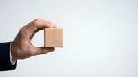 Close-up of male hand in business suit holding blank wooden cube against white background for branding, mockup, or corporate messaging concepts.