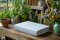 White blank book on rustic wooden table surrounded by potted plants and dried flowers in cozy garden setting.