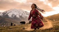 Young Asian woman in traditional red dress dancing joyfully in mountain landscape at sunset with yaks grazing in background for cultural celebration content.