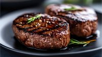 Grilled beef tenderloin steaks with rosemary garnish on dark plate, juicy meat with charred grill marks and seasoning, close up view for restaurant menu.