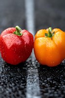 Fresh red and orange bell peppers with water drops on dark background, macro shot showing vibrant colors and texture for food photography and culinary design.