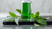 Green herbal extract in glass bottle with fresh mint leaves on dark slate board for natural wellness and aromatherapy applications.