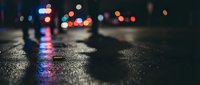 Wet asphalt street at night with colorful bokeh lights reflecting on pavement surface creating atmospheric urban scene for backgrounds and mood concepts.